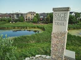 sage creek trail sign showing greenspace surrounding a manmade pond with large newer houses in the background